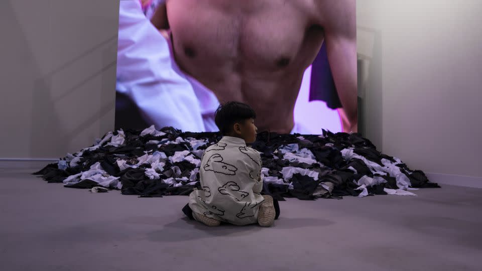 A child sits in front of Japanese artist Fuyuhiko Takata's video work "Cut Suits." - Louise Delmotte/AP