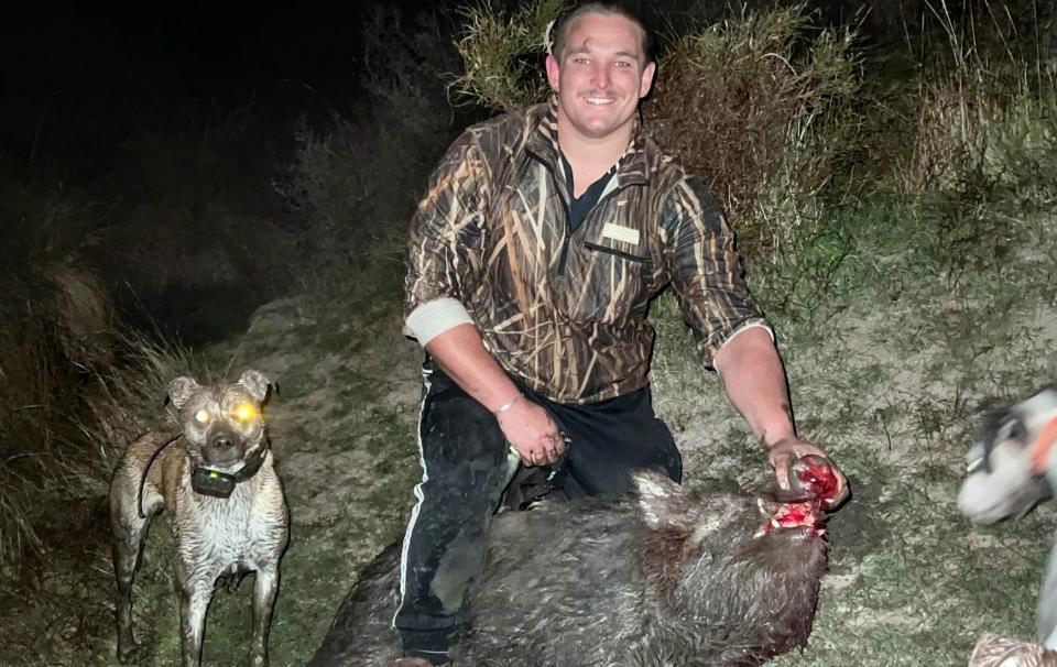 Ethan de Groot with a captured and bleeding pig with his dogs alongside