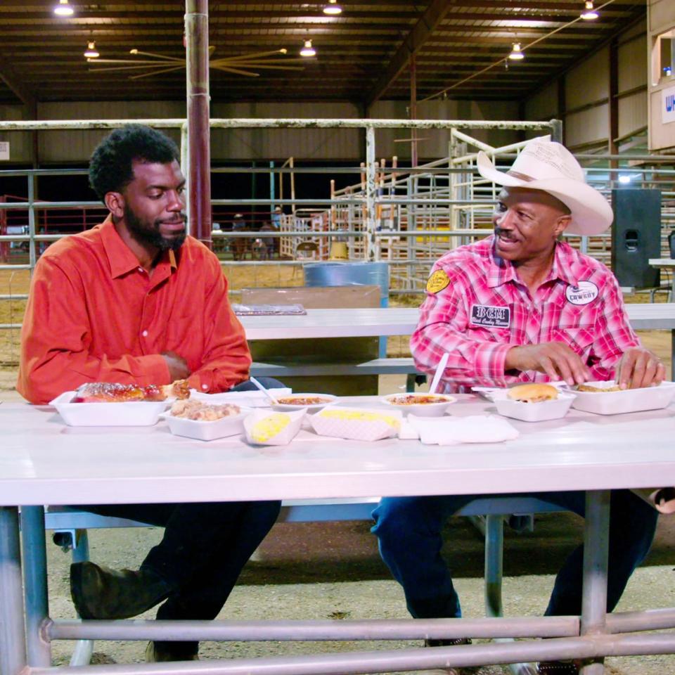 Host Stephen Satterfield (left) enjoys Texas barbecue at a rodeo with former country singer Larry Callies in the Netflix series High on the Hog, How African American Cuisine Transformed America.