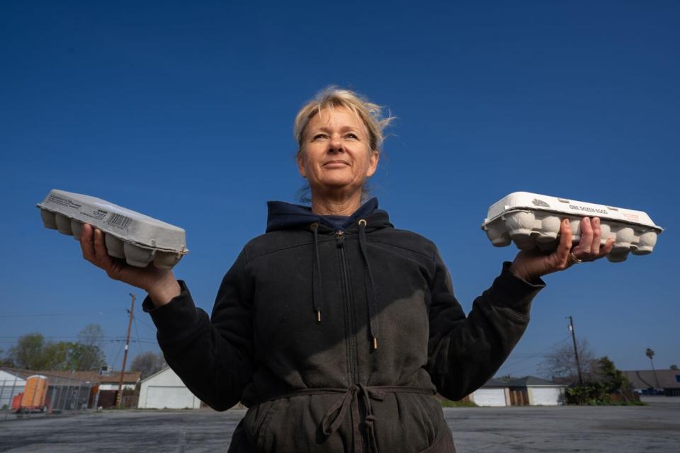 A smiling woman holding a carton of eggs in each hand