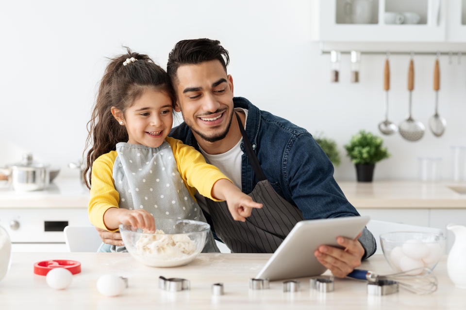 Little Arab Girl And Her Dad Checking Dough Online Recipe On Digital Tablet While Baking Pastry In Kitchen Together, Middle Eastern Father And Daughter Enjoying Cooking At Home, Free Space