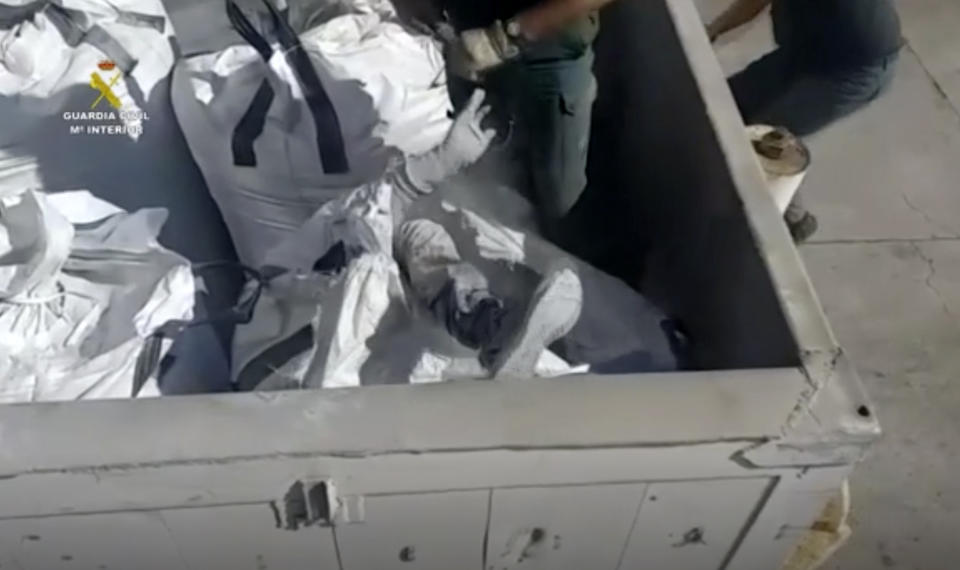 In this image taken from video made available by the Guardia Civil, an officer of the Guardia Civil helps a man out from a bag of ashes in a container in Melilla, Spain, Friday Feb. 19, 2021. Spanish authorities say they have found and rescued 41 migrants who tried to reach continental Europe from North Africa in the past four days, some of them hiding inside a container of discarded glass bottles and a bag of toxic ash. (Guardia Civil via AP)