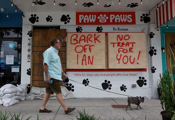 ST. PETERSBURG, FLORIDA - SEPTEMBER 27:  Michael (who didn't want to use their last name) and Romeo walk past a sign reading,' Bark Off Ian, No Treat for you,' painted on a building that is boarded up for the possible arrival of Hurricane Ian on September 27, 2022 in St Petersburg, Florida. Ian is expected in the Tampa Bay area Wednesday night into early Thursday morning. (Photo by Joe Raedle/Getty Images)