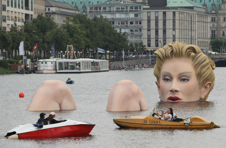 People in boats approach "Die Badende" ("The Bather"), a giant sculpture showing a woman's head and knees as if she were resting in the Binnenalster lake on August 3, 2011 in Hamburg, Germany. The sculpture, which is made of styrofoam and steel and measures 4 meters high and 30 meters long, is a project by artist Oliver Voss and will be on display for the next ten days. 