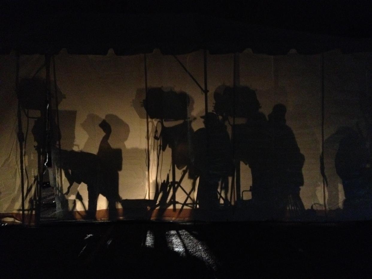 An image of shadows shows a cable news production staff breaking down their set for the night behind a tent.