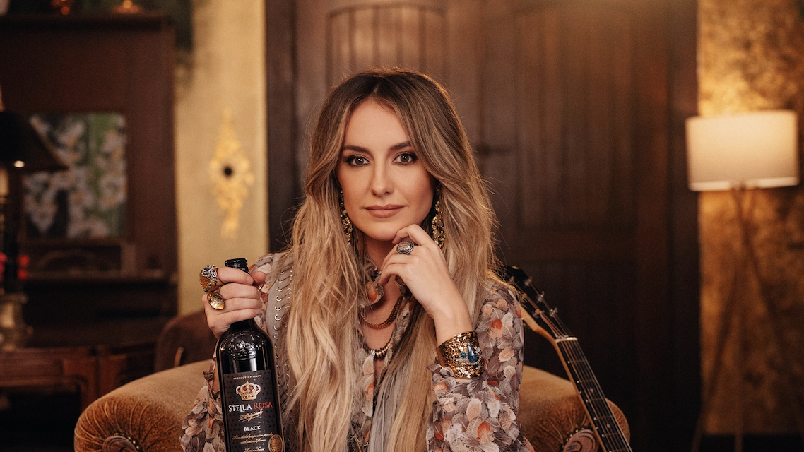 a woman sitting in a chair holding a bottle of wine and a guitar