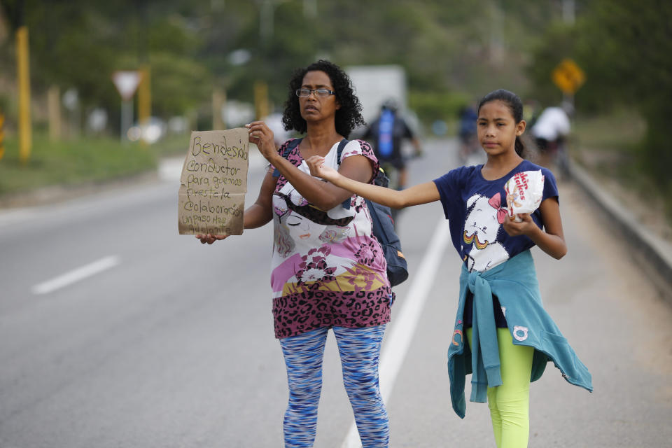 In this Sept. 2, 2018 photo, Venezuelan Sandra Cadiz holds up her handmade sign carrying the Spanish message: "Blessed driver, please help us with a ride," as her 10-year-old daughter Angelis stands with her on the road leaving Giron, Colombia, as they make their way to Peru. As rising numbers of Venezuelans flee, those who cannot afford a plane or bus ticket out are going by foot. (AP Photo/Ariana Cubillos)