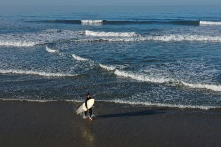A surfer walks out of the Pacific Ocean at sunrise on the 50th anniversary of Earth Day, as the global outbreak of coronavirus disease (COVID-19) continues, in Huntington Beach