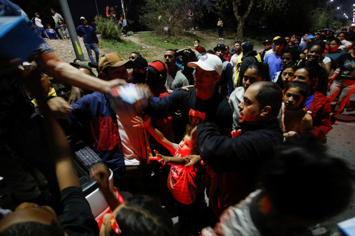 A crowd of migrants hold out their hands for food.