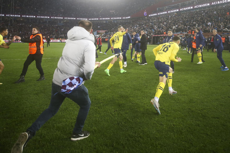 A Trabzonspor supporter swings a corner flag towards Fenerbahce's Mert Muldur, right, during clashes at the end of Turkish Super Lig soccer match between Trabzonspor and Fenerbahce at the Senol Gunes stadium in Trabzon, Turkey, Sunday, March 17, 2024. Turkish top tier club Trabzonspor fans invaded the pitch following a home loss against Fenerbahce late Sunday, touching off violent scuffles between the fans and Fenerbahce players. (Huseyin Yavuz/Dia Images via AP)