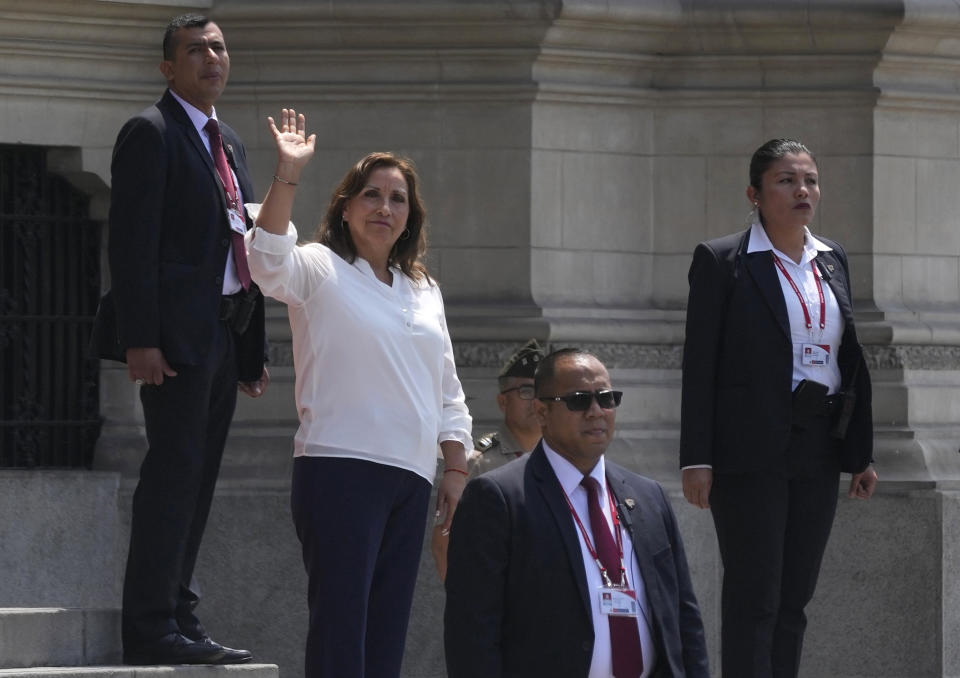 Surrounded by security, Peruvian President Dina Boluarte waves to the press outside the government palace as Prime Minister Alberto Otarola departs in Lima, Peru, Tuesday, Jan. 10, 2023. (AP Photo/Martin Mejia)