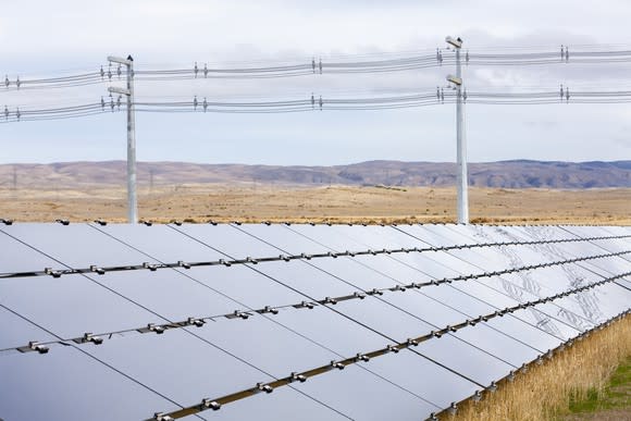 Row of solar panels in an arid open landscape with transmission lines right behind the array.