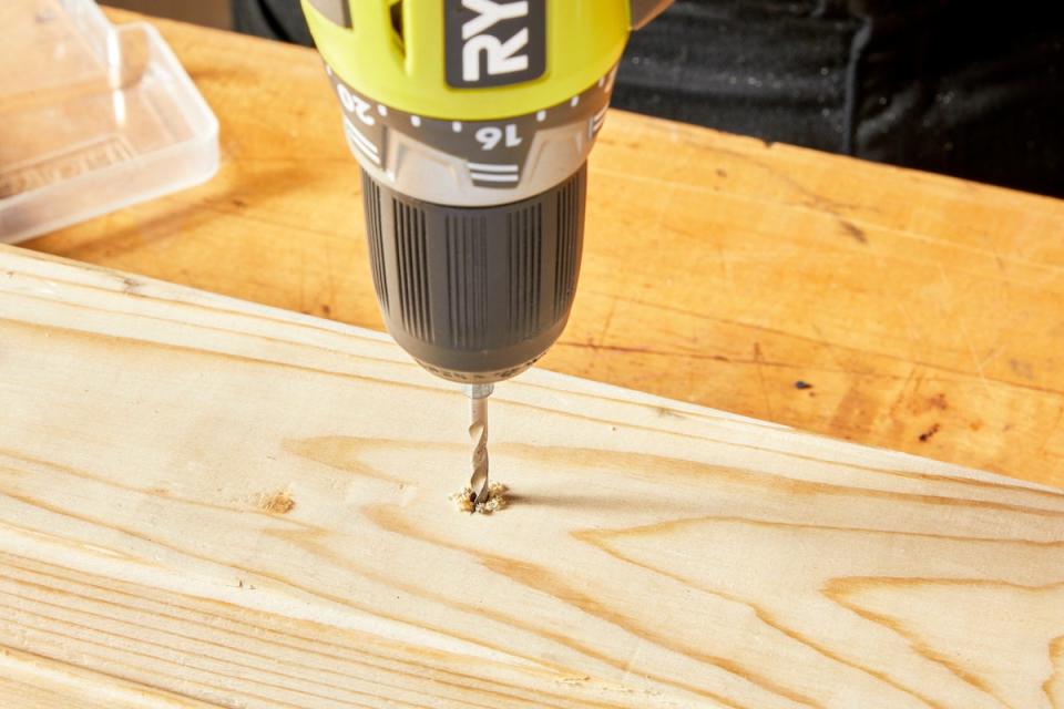 Man pushes drill bit through a piece of wood.