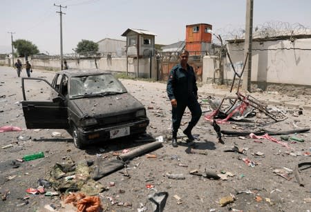 An Afghan police officer walks past a damaged car at the site of a blast in Kabul, Afghanistan