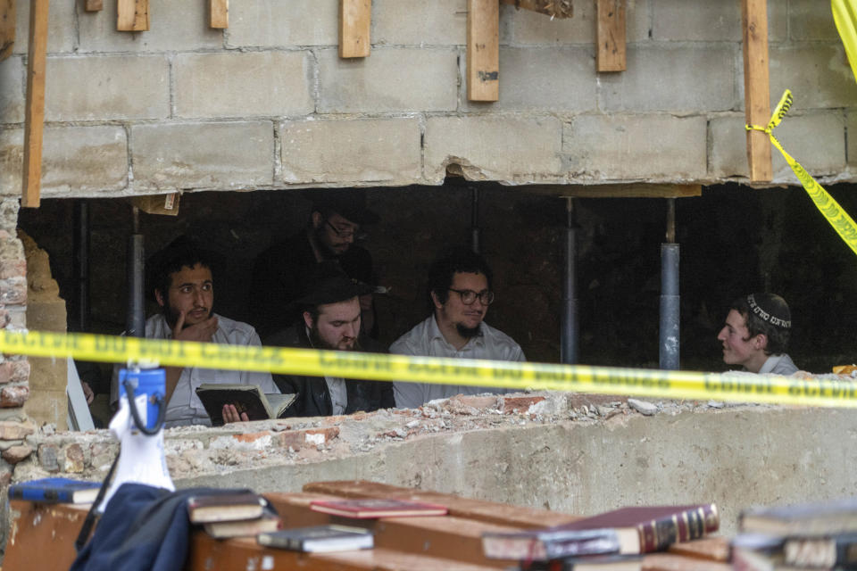 Hasidic Jewish students sit behind a breach in the wall of a synagogue that led to a tunnel dug by the students, Monday, Jan. 8, 2024, in New York. A group of Hasidic Jewish worshippers were arrested amid a dispute over a secret tunnel built beneath a historic Brooklyn synagogue, setting off a brawl between police and those who tried to defend the makeshift passageway. (Bruce Schaff via AP)