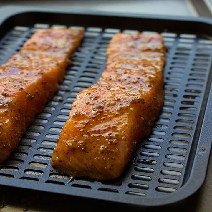 Two pieces of marinated salmon in an air fryer.