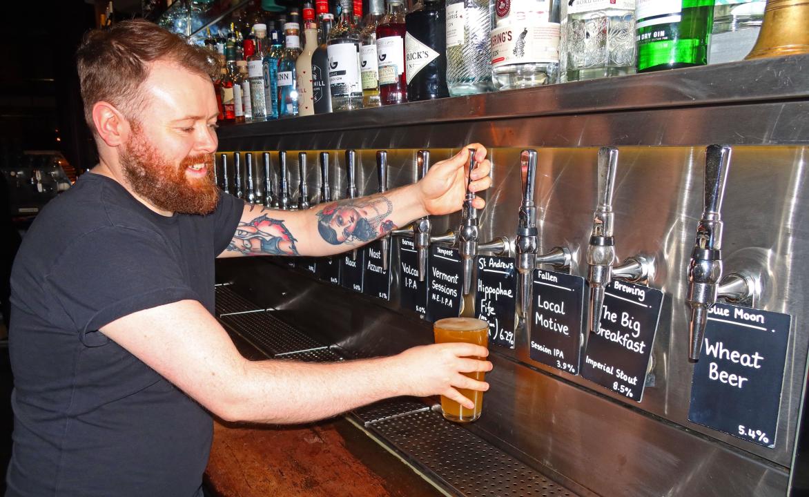 Smiling Barman pulling a pint, in a craft beer bar, with many craft beer taps, Edinburgh, Scotland, UK