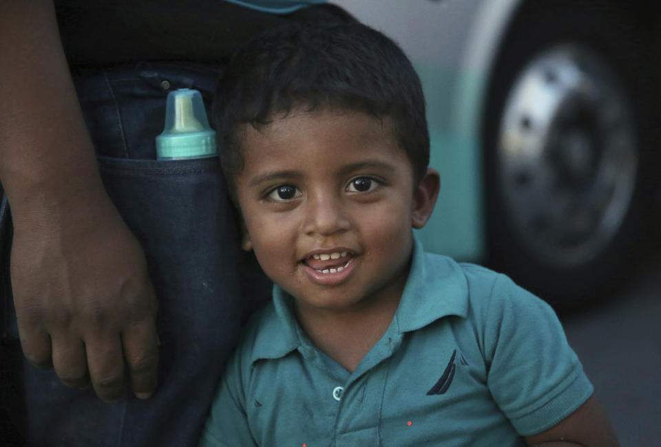 In this July 16, 2019 photo, a migrant child looks at the camera as he waits with his family, outside at an immigration center on the International Bridge 1, to be bused from Nuevo Laredo to Monterret, Mexico. Mexican President Andres Manuel Lopez Obrador's government did not mention the bused migrants Monday when it presented a report halfway into a 90-day period during which it has agreed to reduce irregular trans-migration as part of a deal to head off threatened U.S. tariffs. (AP Photo/Marco Ugarte)