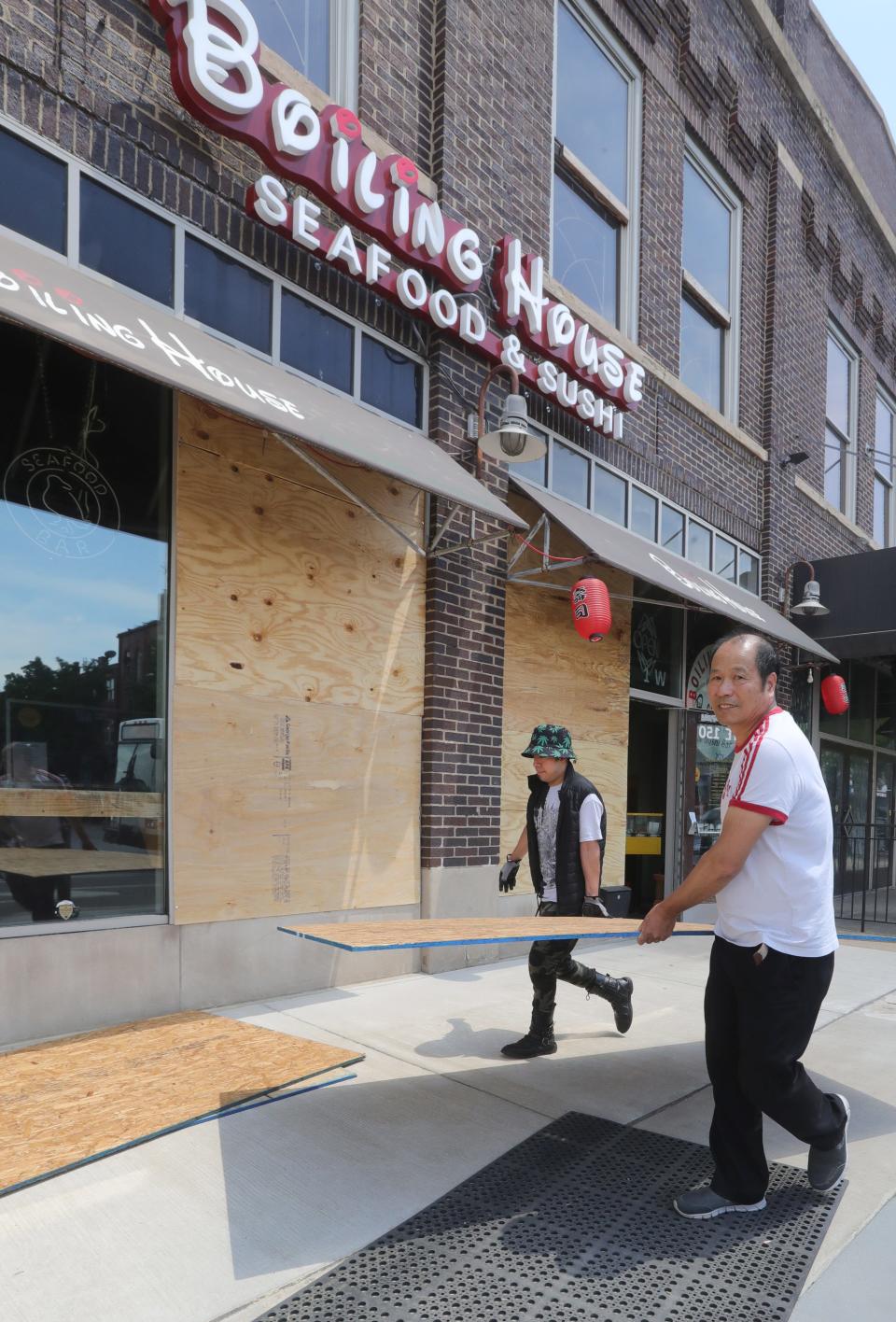 Workers carry plywood Monday to board up the windows of Boiling House in Akron. The restaurant was damaged during unrest downtown Sunday night.