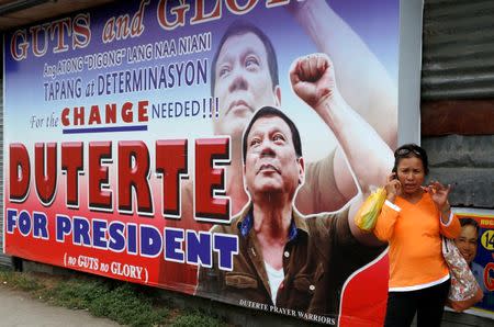 A resident talks on her mobile phone beside a huge election campaign poster of leading presidential candidate Rodrigo "Digong" Duterte in Davao city, southern Philippines, May 11, 2016. REUTERS/Erik De Castro