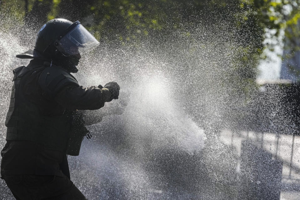 A police officer is splashed with water from a police water cannon as he prepares to throw a tear gas canister during a protest marking the fourth anniversary of anti-government protests, in Santiago, Chile, Wednesday, Oct. 18, 2023. (AP Photo/Esteban Felix)