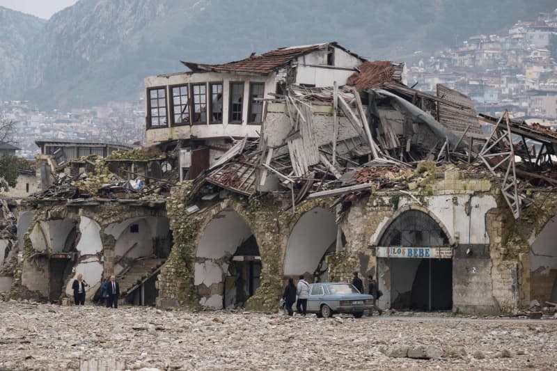 People walk past destroyed houses in the old town of Antakya. Numerous houses in the city center were destroyed or severely damaged in the quake a year ago. Boris Roessler/dpa