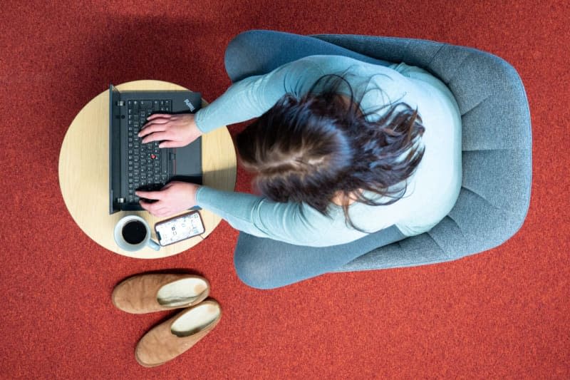 A woman sits in an armchair in her home office and works on a laptop (staged scene). Sebastian Kahnert/dpa