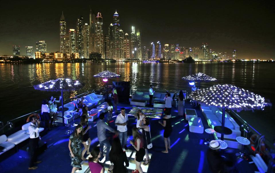 FILE - Guests dance on the GuGu boat during a private party with the skyline of the Marina Waterfront in Dubai, United Arab Emirates, on April 22, 2015. The FIFA World Cup may be bringing as many as 1.2 million fans to Qatar, but the nearby flashy emirate of Dubai is also looking to cash in on the major sports tournament taking place just a short flight away. (AP Photo/Kamran Jebreili, File)