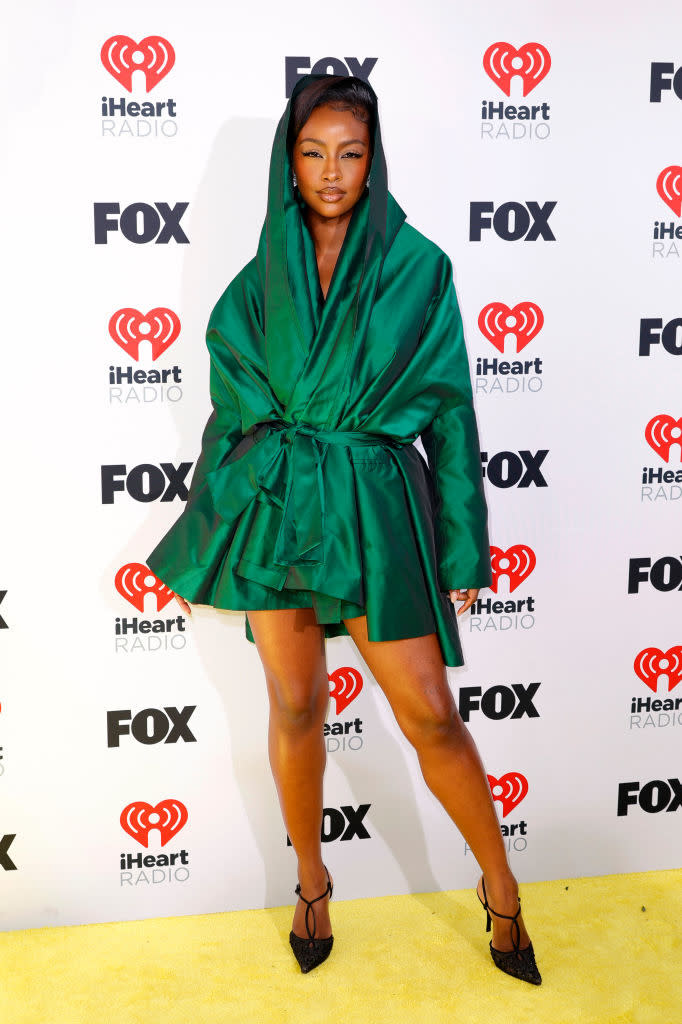 Celebrity in a hooded, belted mini dress and heels posing on the event's photo backdrop