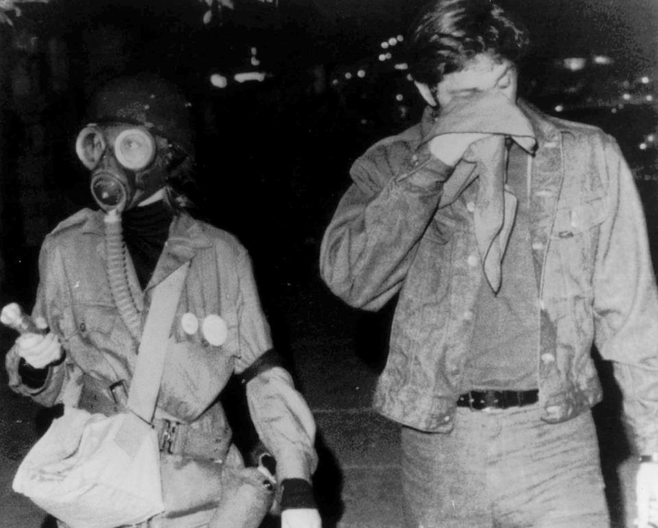 FILE - In this Aug. 27, 1968, file photo, a woman wears a gas mask as she walks with a companion holding a cloth to his eyes after they were sprayed with tear gas during protests on Chicago's North Side. The Associated Press found that there is no government oversight of the manufacture and use of tear gas. Instead, the industry is left to regulate itself. (AP Photo/File)