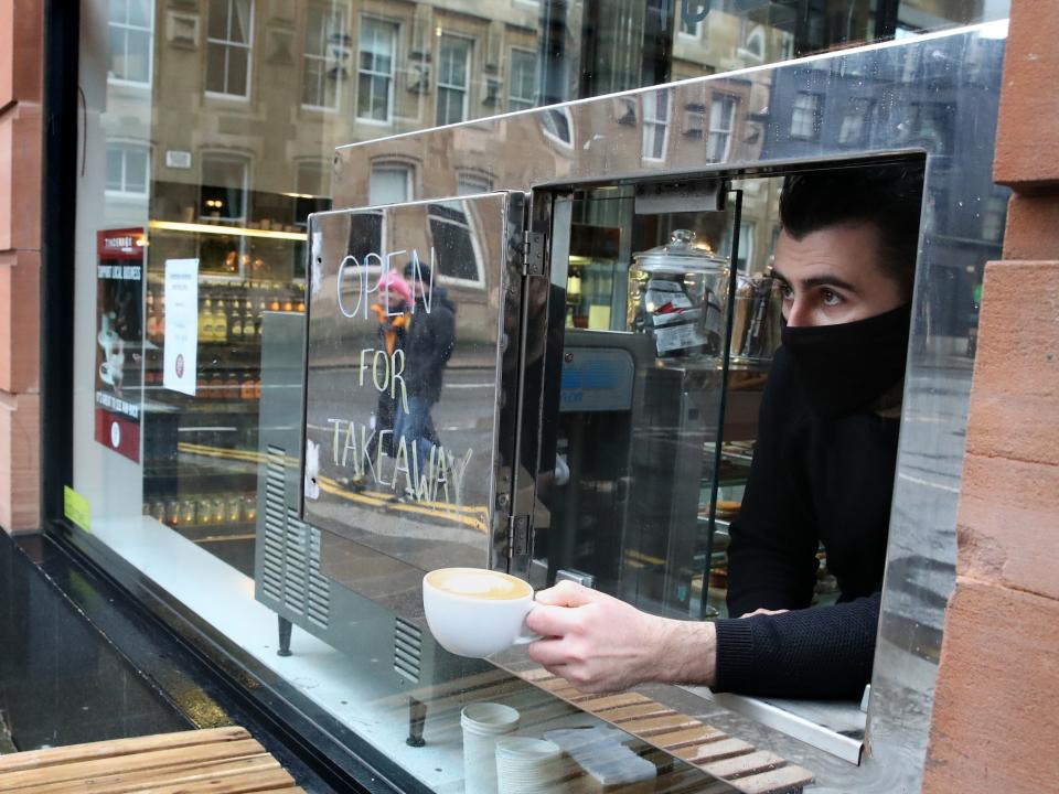 <p>A member of staff looks out from a serving hatch at the Tinderbox coffee shop in Glasgow, as stricter lockdown measures have came into force for mainland Scotland</p> (PA)