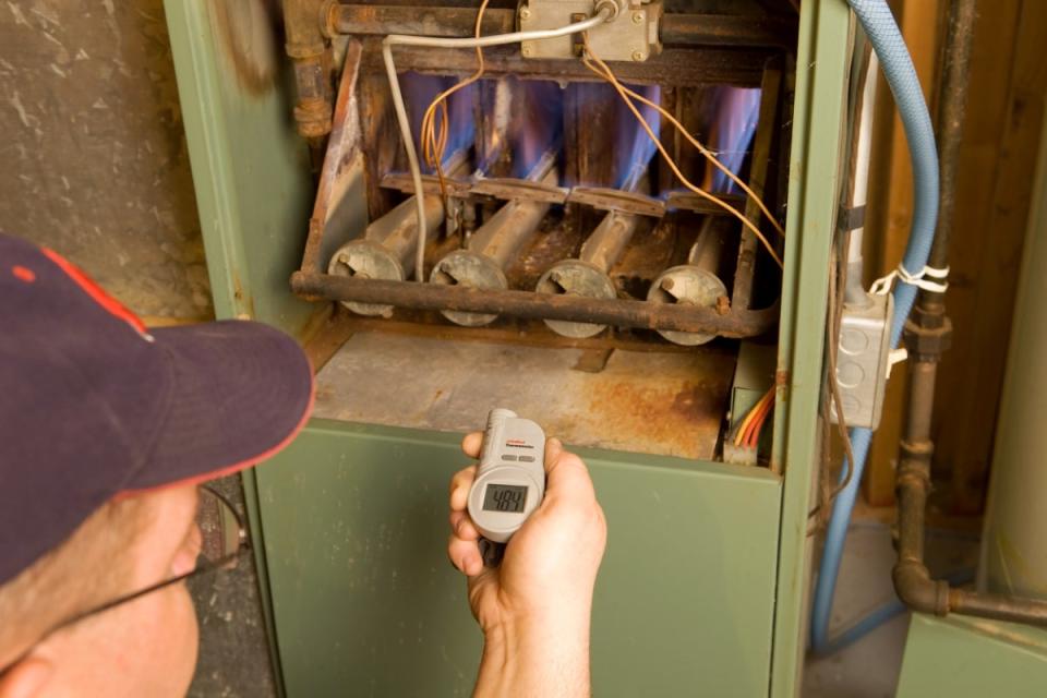 Man checking temperature on gas furnace pilot light.