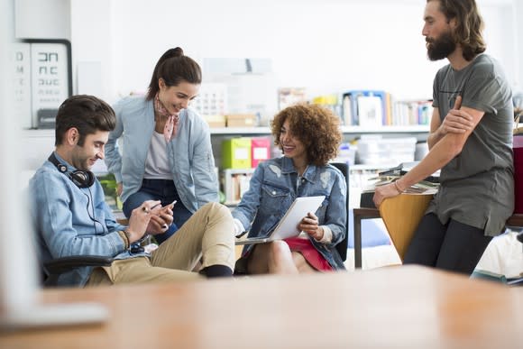 Young adults gathered around a table smiling and using devices