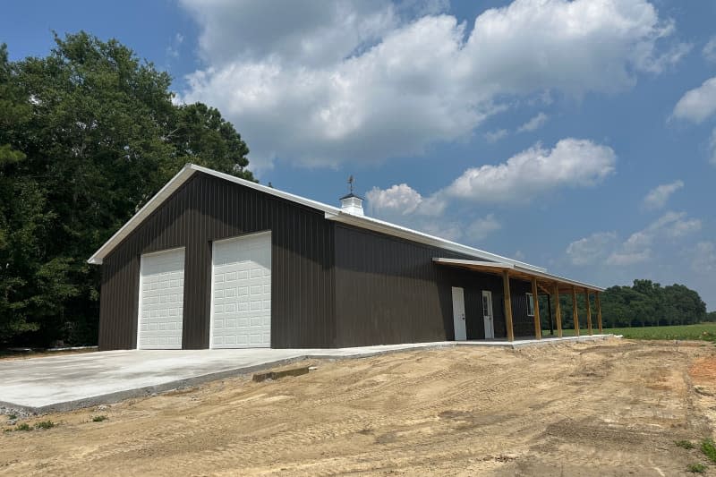 Post frame building pole barn or barndominium with two roll-up doors, concrete floor, metal siding and roofing, lean-to and cupola