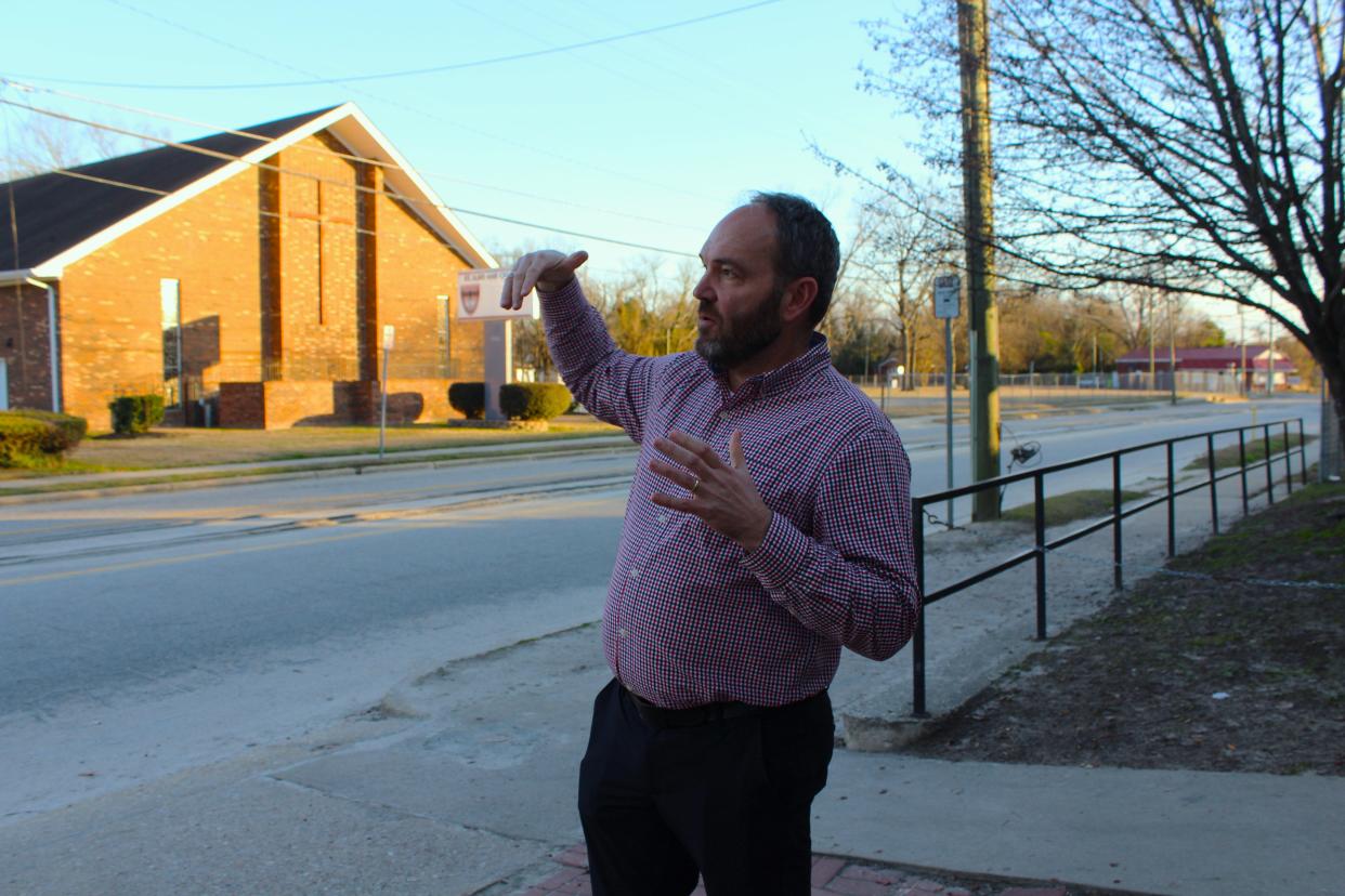 Craig Morrison gestures across the street from the Fayetteville Area Operation Inasmuch shelter, explaining how the shelter bought adjacent land and plans to build transitional housing options for women and children in the city, which it lacks.