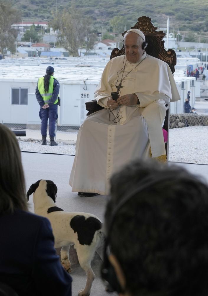 Pope Francis smiles as a stray dog stands in front of him during a ceremony at the Karatepe refugee camp, on the northeastern Aegean island of Lesbos, Greece, Sunday, Dec. 5, 2021. Pope Francis is returning to Lesbos, the Greek island that was at the heart of a massive wave of migration into Europe. (AP Photo/Alessandra Tarantino)
