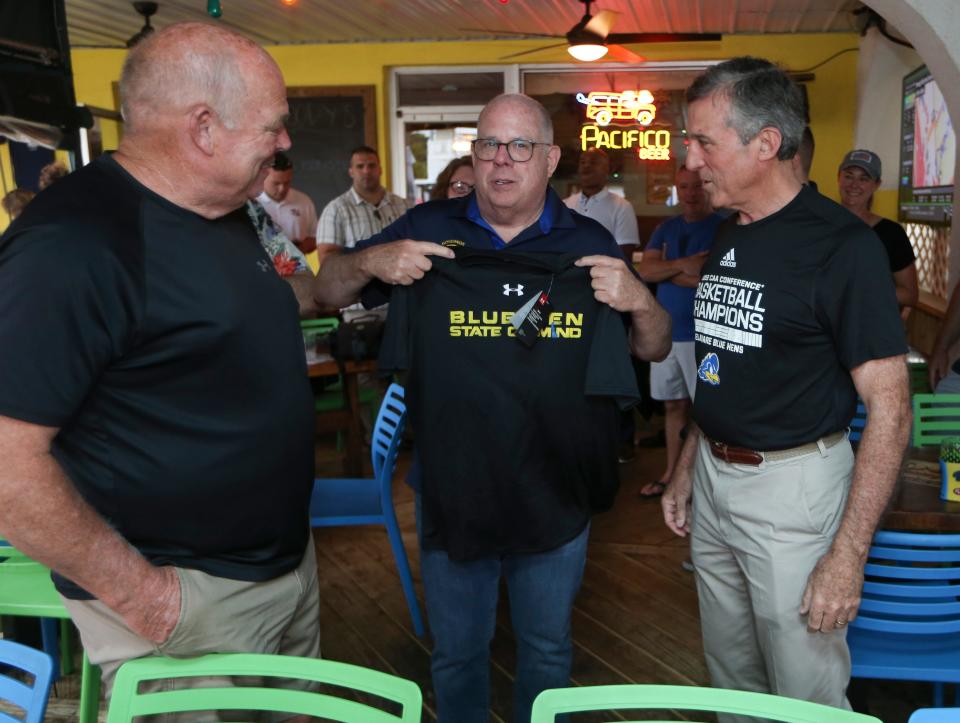 Maryland Governor Larry Hogan (center) receives some Delaware swag from Gov. John Carney (right) as Speaker of the Delaware House of Representatives Peter Schwartzkopf looks on Sunday, June 12, 2022, at Woody's restaurant in Dewey Beach. Carney was fulfilling his end of a NCAA women's basketball tournament wager by hosting a crabcake lunch.