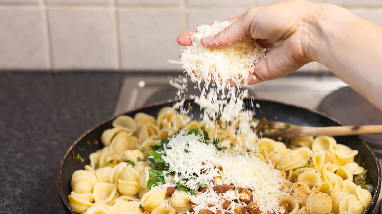 hand sprinkling grated parmesan cheese into pasta pan
