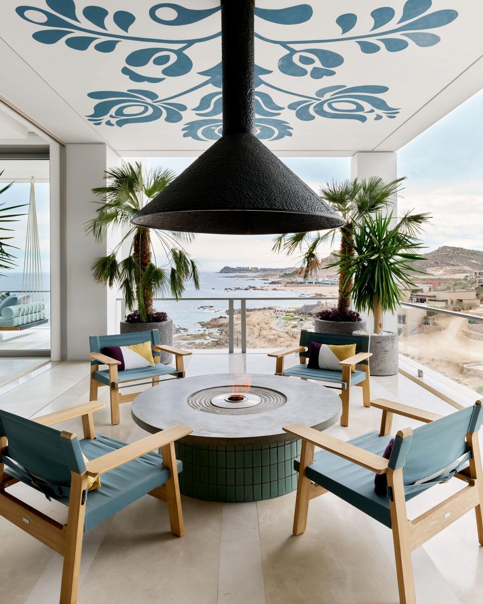 On a terrace, local artist Daniela Medina painted a ceiling mural in Benjamin Moore's Philipsburg Blue. Armchairs by Martyn Lawrence Bullard for Harbour 1976 wear an indoor/outdoor fabric by Holly Hunt; bespoke fireplace.