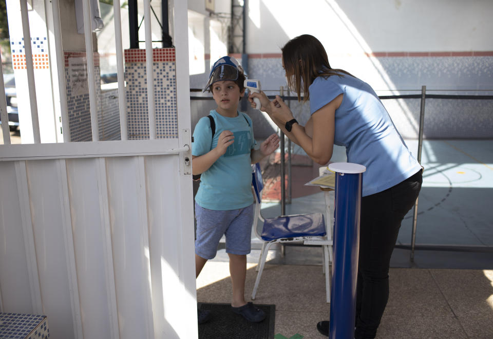 A teacher checks the temperature of Bernardo Santo as he arrives at the Pereira Agustinho daycare, nursery school and pre-school, after it reopened amid the new coronavirus pandemic in Duque de Caxias, Monday, July 6, 2020. The city of Manaus in the Amazon rainforest and Duque de Caxias in Rio de Janeiro’s metropolitan region, became on Monday the first Brazilian cities to resume in-person classes at private schools since the onset of the COVID-19 pandemic, according to the nation's private school federation. (AP Photo/Silvia Izquierdo)