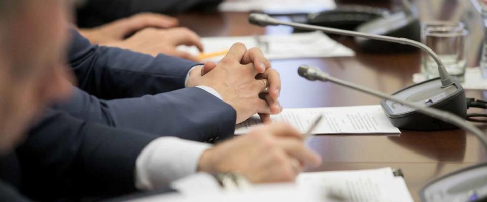 One of politician sitting by table with his hands over document during political summit or conference