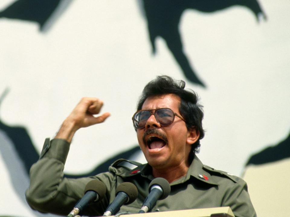 Daniel Ortega in 1984 shouting into a microphone in front of a massive mural.