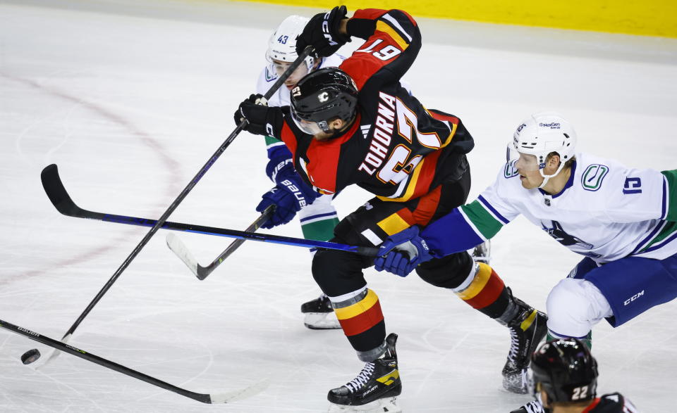 Vancouver Canucks defenseman Quinn Hughes, left, and forward Sheldon Dries, right, check Calgary Flames forward Radim Zohorna during the first period of an NHL hockey game in Calgary, Alberta on Wednesday, Dec. 14, 2022. (Jeff McIntosh/The Canadian Press via AP)