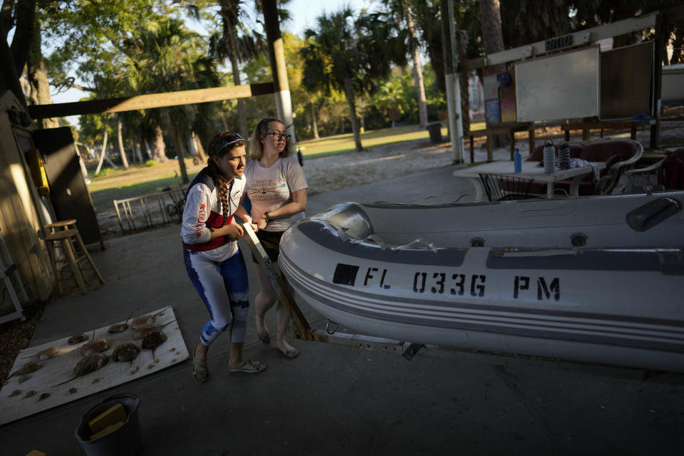 Antonia Ginsberg-Klemmt, 23, left, a physics major who started a rowing team at New College of Florida, gets help from team member Kaitlin Kelleher to stow the boat she uses to coach practice, at the end of a morning training session, Thursday, March 2, 2023, in Sarasota, Fla. Ginsberg-Klemmt, who is graduating this spring, says she has stayed away from campus protests and is trying to focus on her senior thesis, but notices the effect the takeover is having on her peers. "There's a lot less morale," she says. (AP Photo/Rebecca Blackwell)