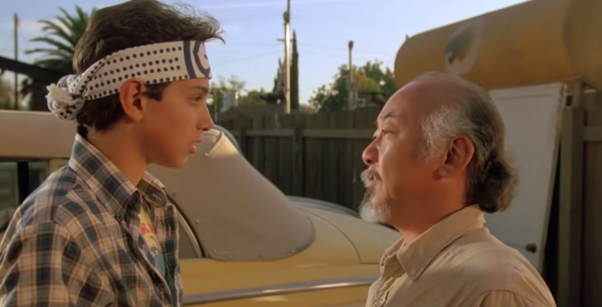 Ralph Macchio standing in front of the yellow 1947 Ford in "The Karate Kid"