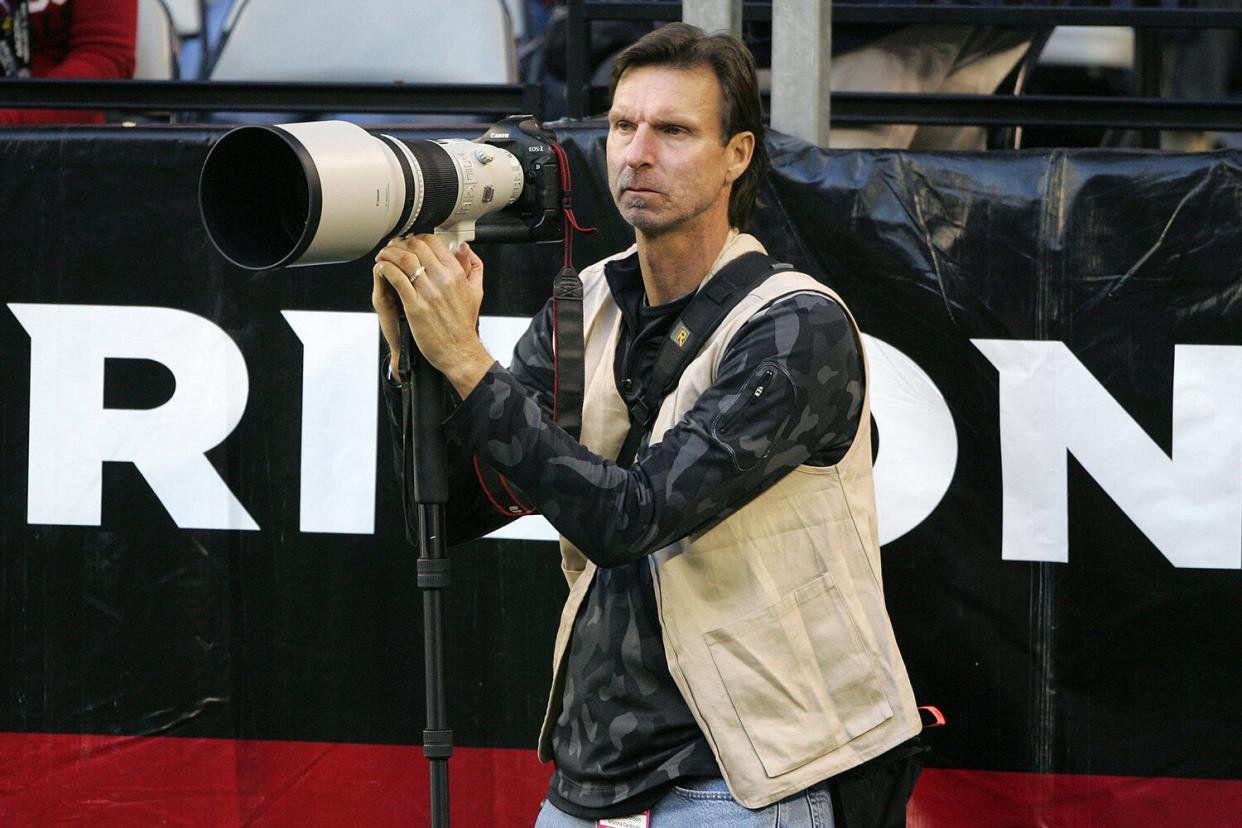 Former MLB pitcher Randy Johnson on sidelines with camera during Dallas Cowboys vs Arizona Cardinals game at University of Phoenix Stadium.