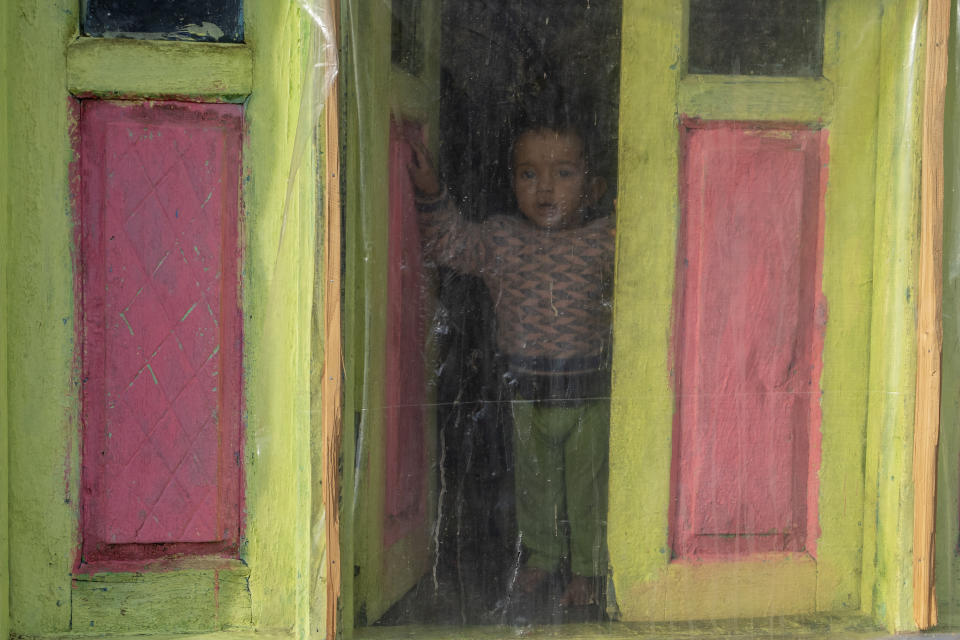 A Kashmiri villager boy looks out of a window covered with a plastic sheet, used as a shield against the cold, in Drang village northwest of Srinagar, Indian controlled Kashmir Friday, Dec. 22, 2023. (AP Photo/Dar Yasin)