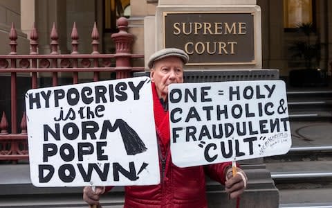 A protester holds placards opposing the Catholic Church outside the Victorian Supreme court where Australian Cardinal George Pell has a hearing in Melbourne - Credit: AFP