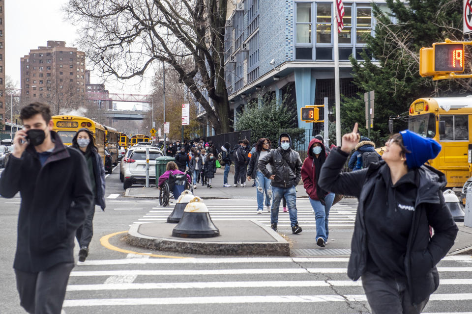 Pedestrians cross Houston Street as students wearing masks leave the New Explorations into Science, Technology and Math (NEST+m) school in the Lower East Side neighborhood of Manhattan on Tuesday, Dec. 21, 2021, in New York. (AP Photo/Brittainy Newman)