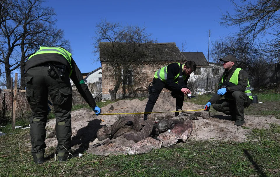 Three inspectors work with volunteer body collectors at an improvised burial site in Irpin on April 14. 